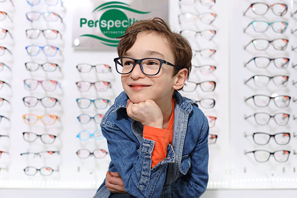Child wearing stylish eye glasses in front of a a selection of children's eye-glass frames
